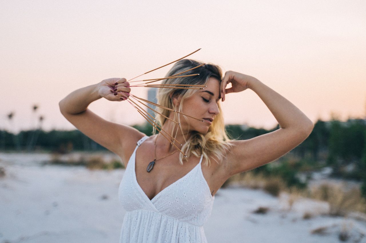 Woman meditating on the beach with incense sticks, embracing mindfulness and serenity at sunset.
